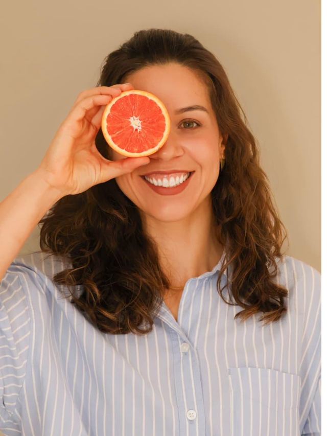 Ana Maria sorrindo, segurando meia toranja próxima ao rosto